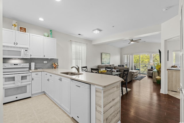 kitchen featuring a peninsula, white appliances, light countertops, a sink, and vaulted ceiling