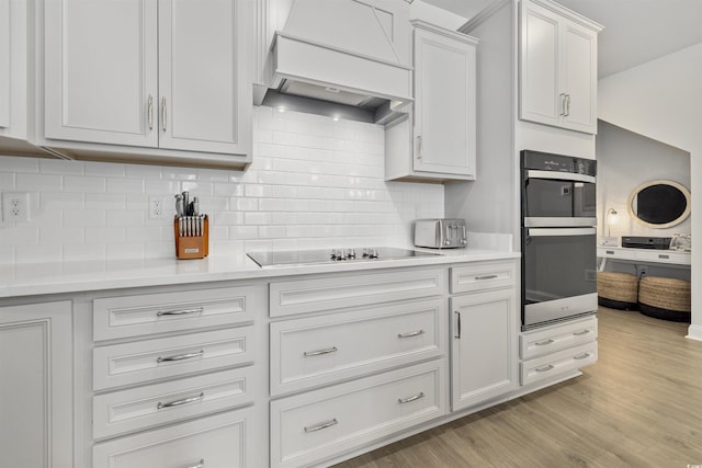 kitchen with backsplash, double wall oven, custom range hood, and black electric cooktop