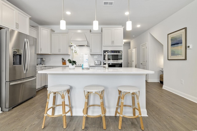 kitchen featuring visible vents, custom exhaust hood, a breakfast bar, appliances with stainless steel finishes, and backsplash