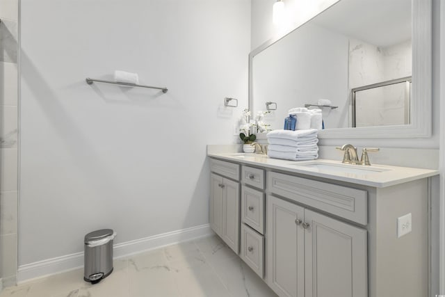 bathroom with double vanity, marble finish floor, baseboards, a shower stall, and a sink