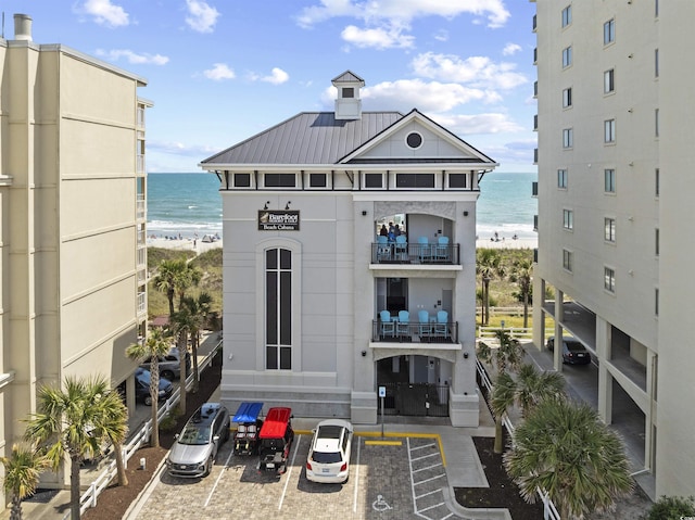 view of building exterior featuring a beach view, a water view, and uncovered parking