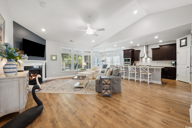 living room with a ceiling fan, high vaulted ceiling, light wood finished floors, a glass covered fireplace, and recessed lighting