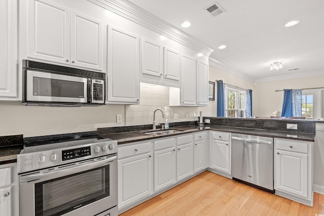 kitchen featuring visible vents, a sink, white cabinets, ornamental molding, and stainless steel appliances