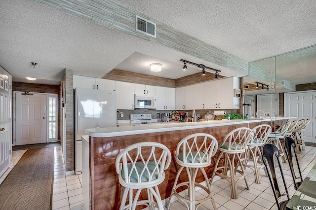 kitchen with a textured ceiling, white appliances, light tile patterned floors, and visible vents