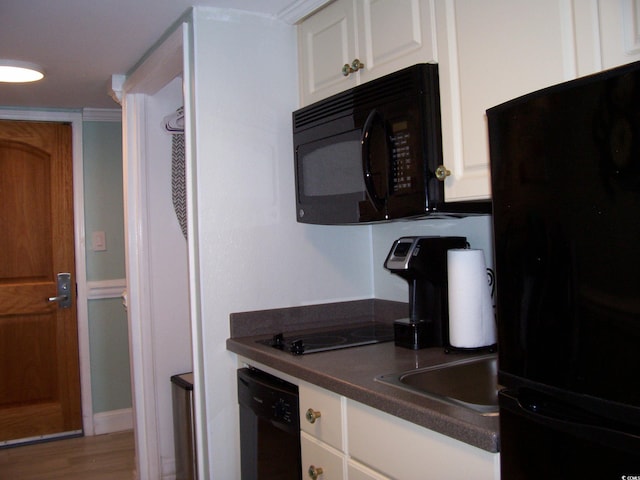kitchen with white cabinets, dark countertops, wood finished floors, and black appliances