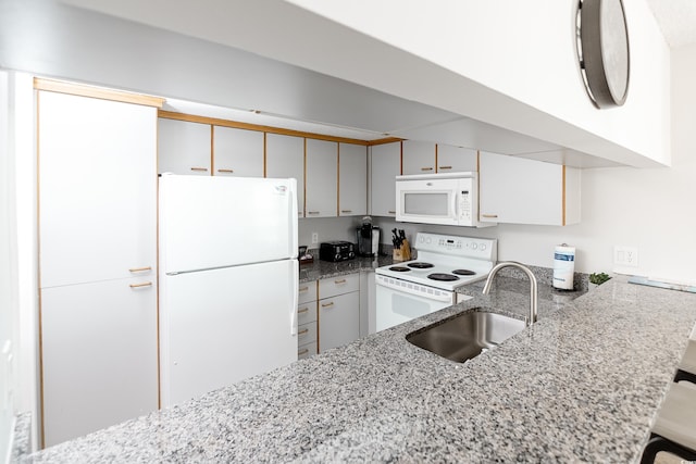 kitchen featuring white appliances, a peninsula, light stone counters, and a sink