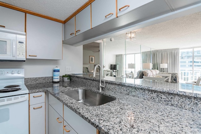 kitchen with white appliances, open floor plan, a textured ceiling, light stone counters, and a sink