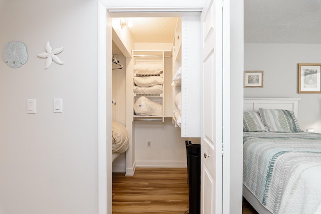 bedroom with baseboards, a textured ceiling, wood finished floors, and a walk in closet