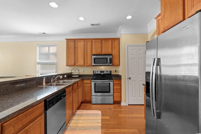 kitchen featuring ornamental molding, a sink, light wood-style floors, dark countertops, and stainless steel appliances