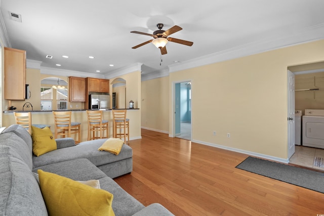 living area with light wood-style flooring, washer and clothes dryer, ceiling fan, arched walkways, and ornamental molding