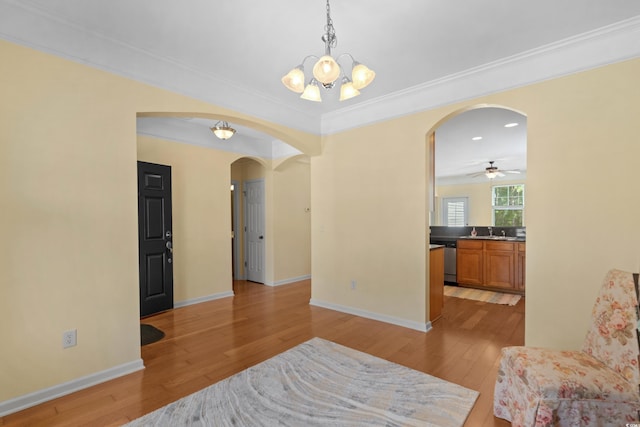 sitting room with ceiling fan with notable chandelier, crown molding, arched walkways, baseboards, and light wood-style floors