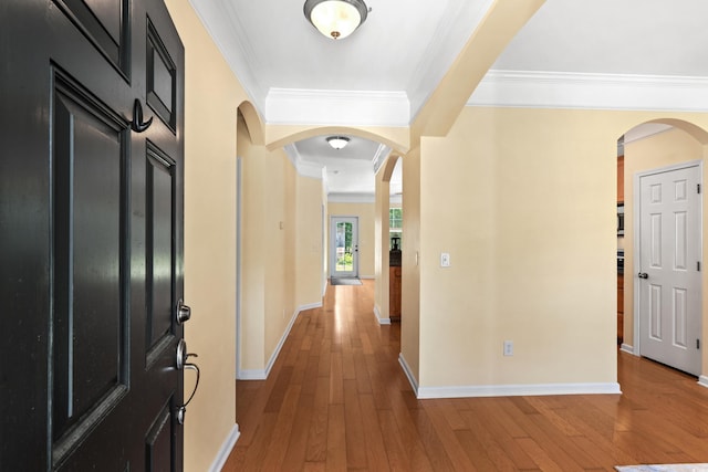 foyer featuring crown molding, hardwood / wood-style flooring, arched walkways, and baseboards