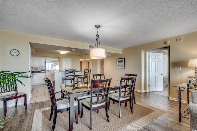 dining area featuring visible vents, a textured ceiling, light wood finished floors, and baseboards
