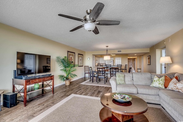 living room featuring a textured ceiling, a ceiling fan, baseboards, wood finished floors, and visible vents