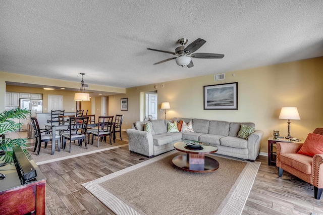 living area with visible vents, a ceiling fan, a textured ceiling, and light wood-type flooring