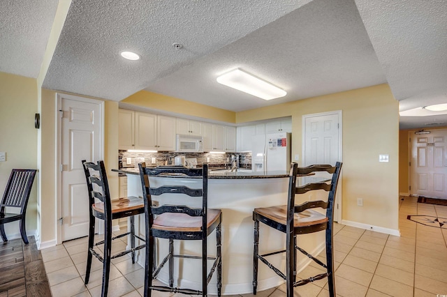 kitchen with white appliances, a kitchen breakfast bar, dark countertops, and a textured ceiling