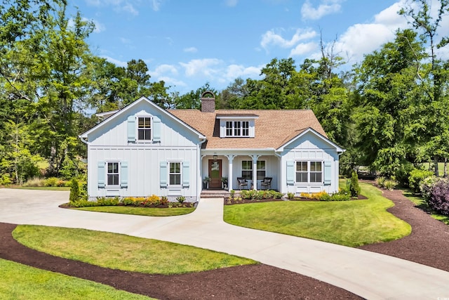 modern farmhouse style home with a chimney, concrete driveway, board and batten siding, a front yard, and a porch