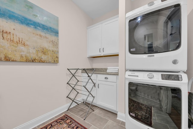 laundry area featuring baseboards, stacked washer and dryer, light tile patterned floors, and cabinet space