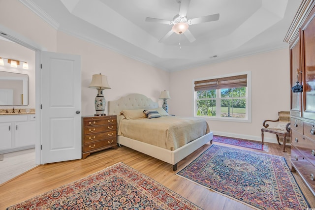 bedroom featuring light wood finished floors, a tray ceiling, crown molding, and a sink