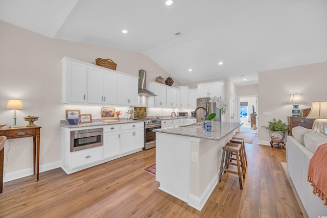 kitchen with a sink, lofted ceiling, wall chimney range hood, white cabinets, and appliances with stainless steel finishes