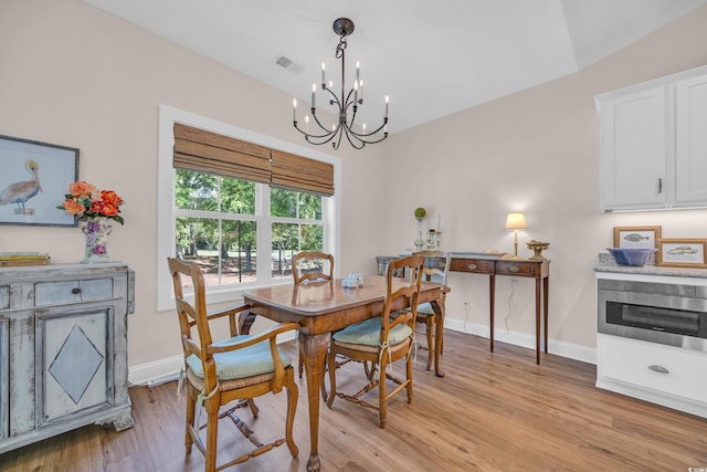 dining space featuring light wood-style floors, a chandelier, baseboards, and visible vents