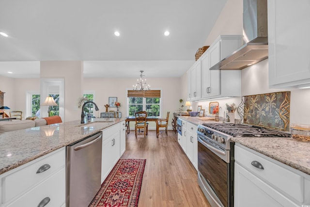 kitchen with a sink, wall chimney range hood, light wood-type flooring, white cabinetry, and appliances with stainless steel finishes