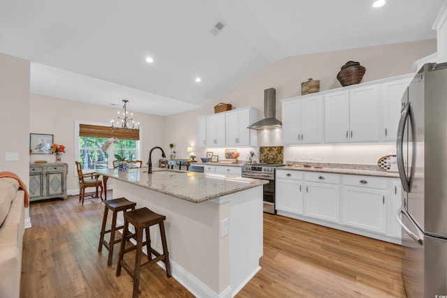 kitchen with lofted ceiling, visible vents, wall chimney exhaust hood, stainless steel appliances, and a kitchen island with sink