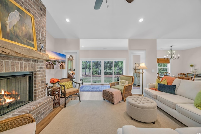 living area with wood finished floors, ceiling fan with notable chandelier, a brick fireplace, and recessed lighting