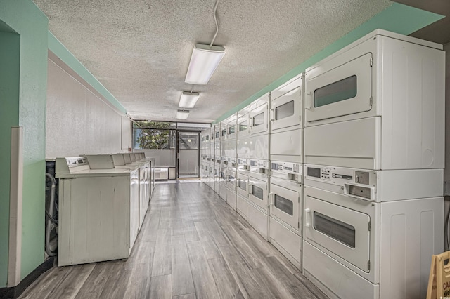 common laundry area with washing machine and clothes dryer, light wood-style floors, stacked washing maching and dryer, and a textured ceiling