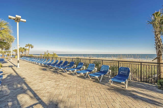 view of patio / terrace featuring fence, a water view, and a beach view