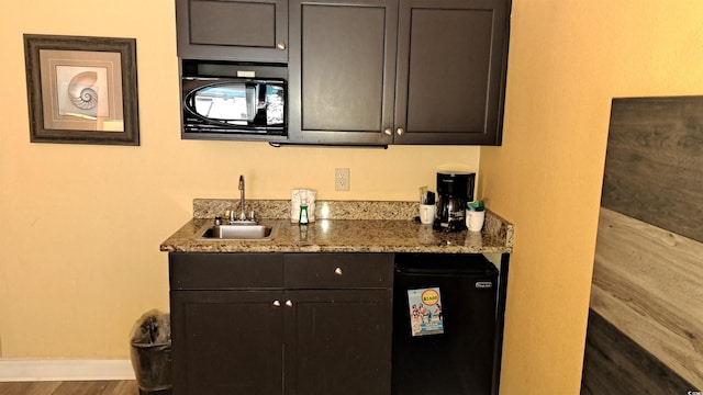 bar featuring baseboards, fridge, a sink, wood finished floors, and indoor wet bar