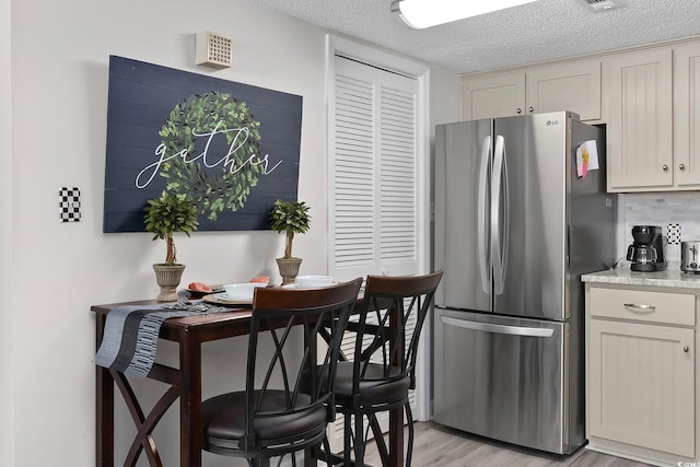 kitchen featuring freestanding refrigerator, a textured ceiling, light countertops, light wood-style flooring, and backsplash