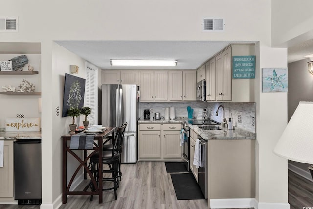 kitchen featuring appliances with stainless steel finishes, light wood-style flooring, light stone countertops, tasteful backsplash, and a textured ceiling
