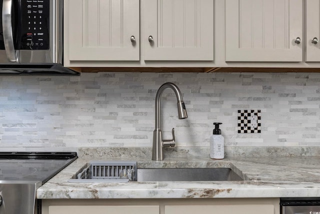 kitchen view of decorative backsplash, stainless steel appliances, a sink, and light stone countertops