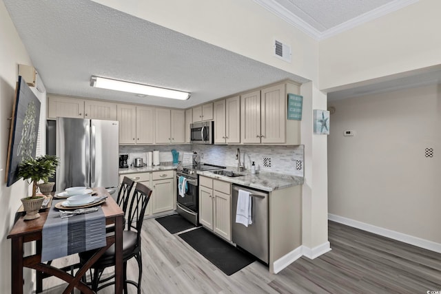 kitchen with stainless steel appliances, a textured ceiling, wood finished floors, crown molding, and tasteful backsplash