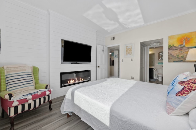 bedroom with wood finished floors, ornamental molding, a glass covered fireplace, and ensuite bath