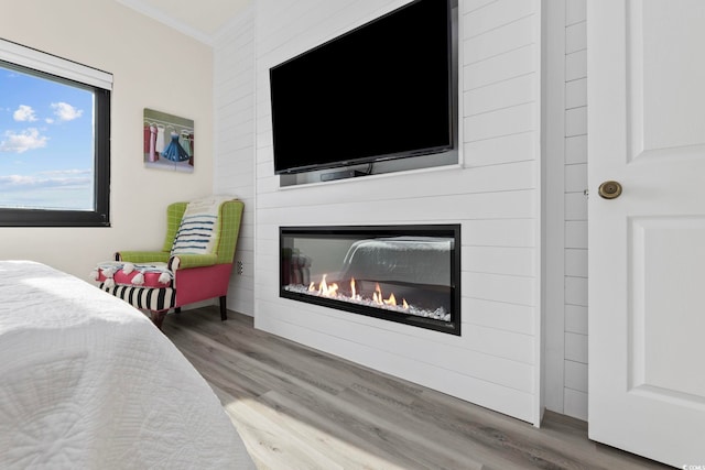 bedroom with wood finished floors, crown molding, and a glass covered fireplace