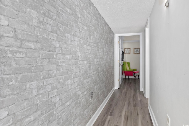 hall featuring a textured ceiling, wood finished floors, and baseboards
