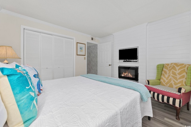 bedroom with crown molding, wood finished floors, a closet, and a fireplace