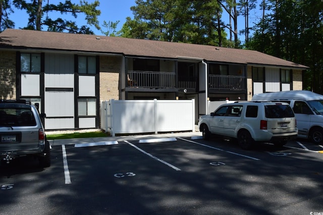 exterior space with brick siding, roof with shingles, fence, and uncovered parking