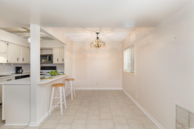 kitchen with visible vents, range with electric stovetop, a breakfast bar area, light countertops, and stainless steel microwave