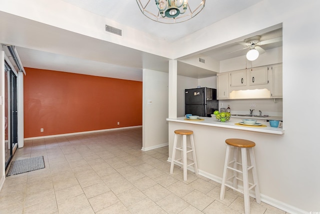 kitchen with a breakfast bar, light countertops, freestanding refrigerator, baseboards, and visible vents