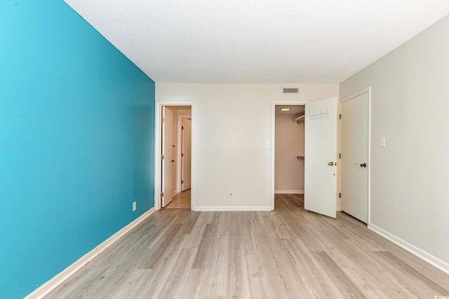 unfurnished bedroom with baseboards, a textured ceiling, light wood-style flooring, and visible vents