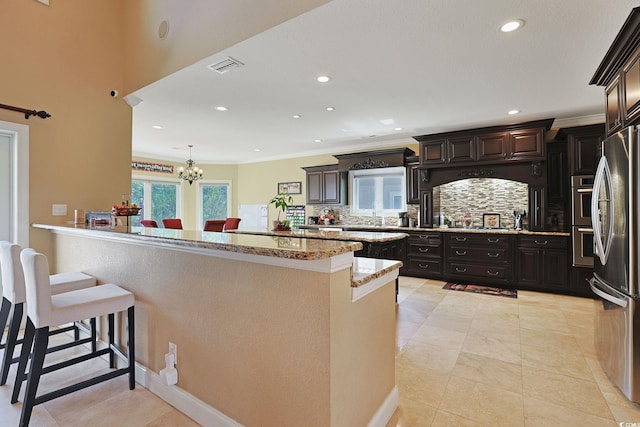kitchen with decorative backsplash, visible vents, light stone counters, a notable chandelier, and stainless steel appliances