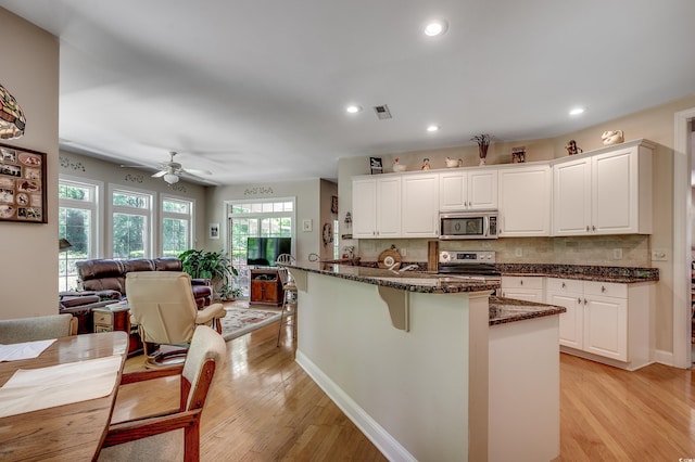 kitchen featuring appliances with stainless steel finishes, light wood-style floors, open floor plan, decorative backsplash, and a kitchen bar
