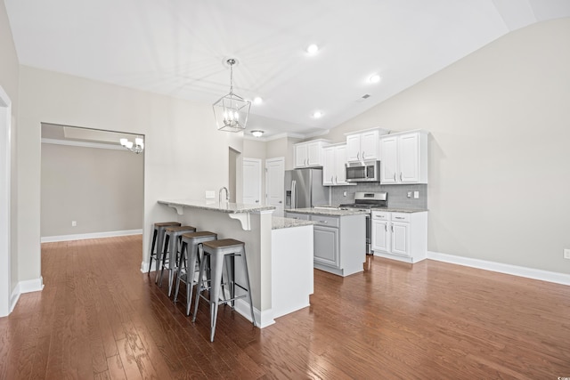 kitchen featuring a kitchen bar, appliances with stainless steel finishes, vaulted ceiling, a peninsula, and a notable chandelier