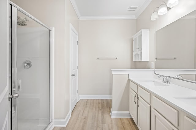 bathroom with a sink, double vanity, a shower stall, wood finished floors, and ornamental molding