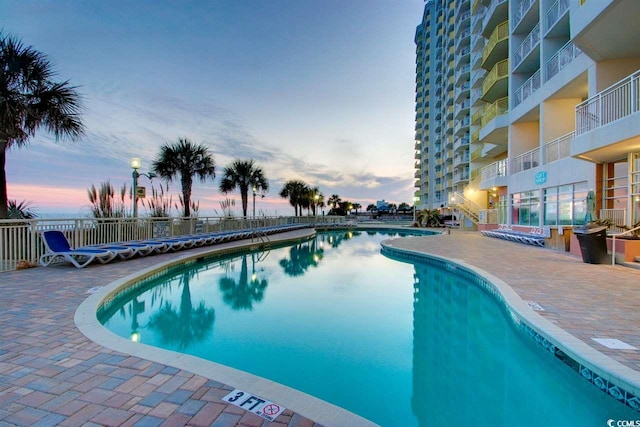 pool at dusk featuring a community pool, fence, and a patio area