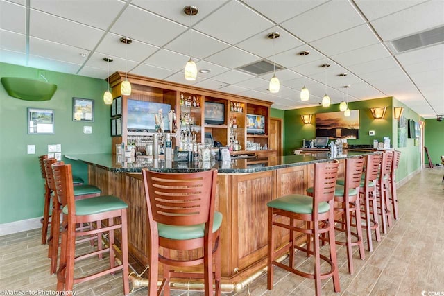 community bar area with a drop ceiling, baseboards, light wood-type flooring, and hanging light fixtures