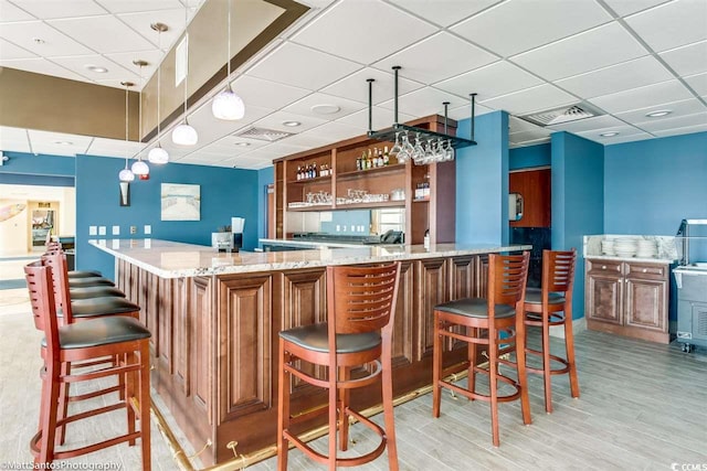 community bar area featuring a drop ceiling, light wood finished floors, and hanging light fixtures